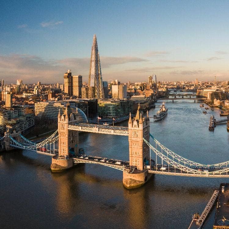 Tower Bridge spans the River Thames with The Shard and London's iconic skyline creating a stunning panoramic cityscape under clear skies.